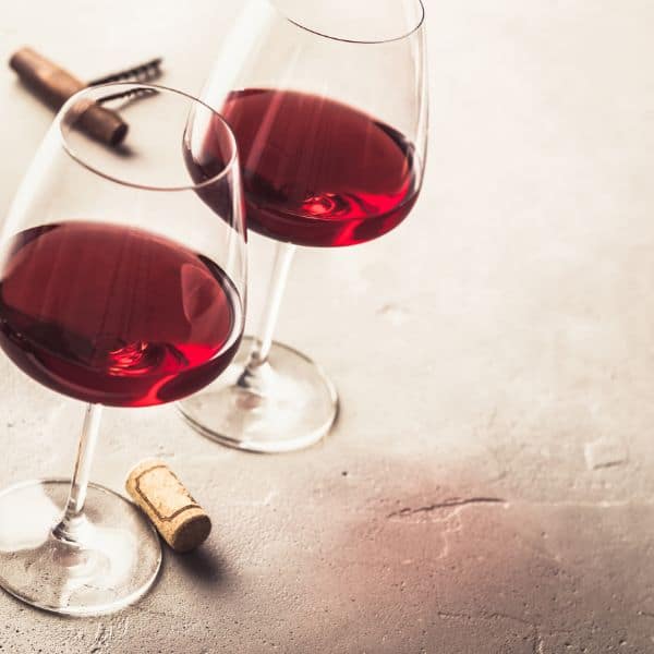 red wine in wine glasses casting a pink shadow with a cork and corkscrew driver lying nearby