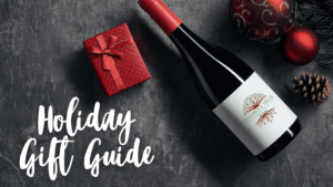 Holiday Gift Guide cover photo with wine bottle, pinecones, evergreen tree branches and a red package